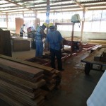 Two guys work the wood planer that strips larger blocks of wood into the outside facings of the boxes.